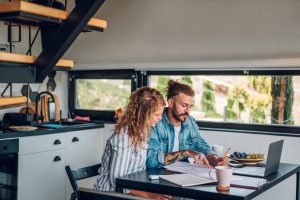 happy-couple-using-laptop-and-looking-into-blueprints-of-their-new-home-e1696858493419.jpg