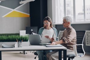 two-confident-women-using-technologies-and-communicating-while-working-in-office-together-e1696735472910.jpg